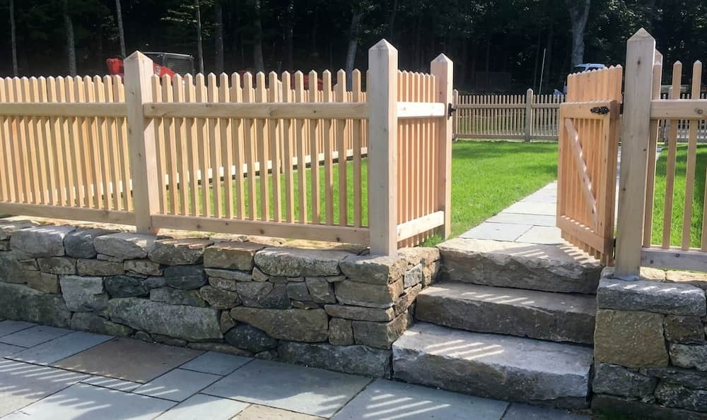 A light-colored wooden picket fence installed atop a natural stone