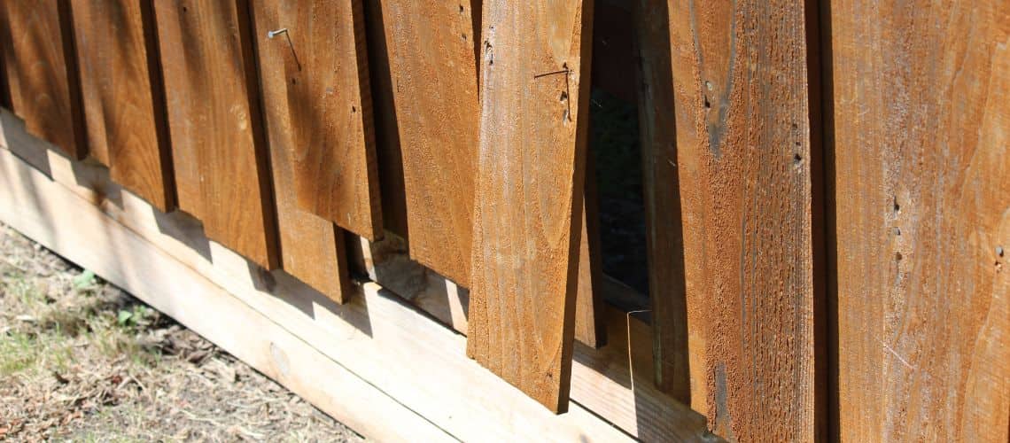 A close-up of a damaged wooden fence with broken and detached vertical slats