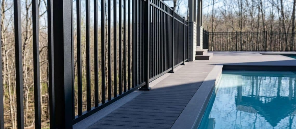 a modern swimming pool bordered by a gray composite deck and a black safety fence