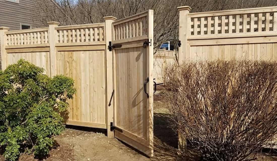 A wooden gate slightly ajar opens to a garden path, flanked by bare shrubs.