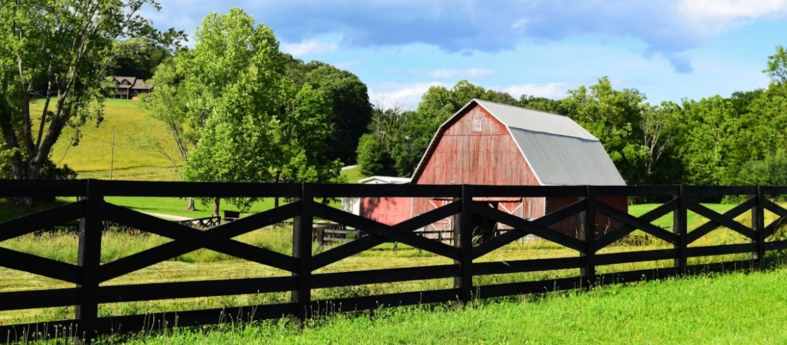 rustic red barn sits behind a black wooden fence